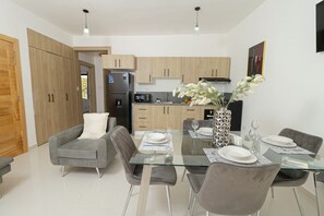 Une cuisine moderne avec des meubles en bois, un réfrigérateur noir et un four à micro-ondes. On y trouve également un coin repas avec une table en verre et des chaises grises.
