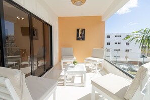 A balcony with white furniture, a small table with a plant, and a painting on the wall.