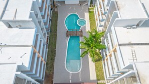 Vue aérienne d’un hôtel moderne doté d’une piscine centrale, entouré de balcons et d’un palmier.