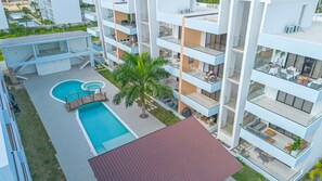 A modern apartment building with a swimming pool, outdoor seating, and balconies.