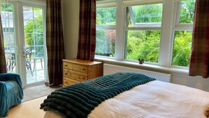 Un dormitorio con cama, cómoda, ventana con cortinas y vista a la vegetación.