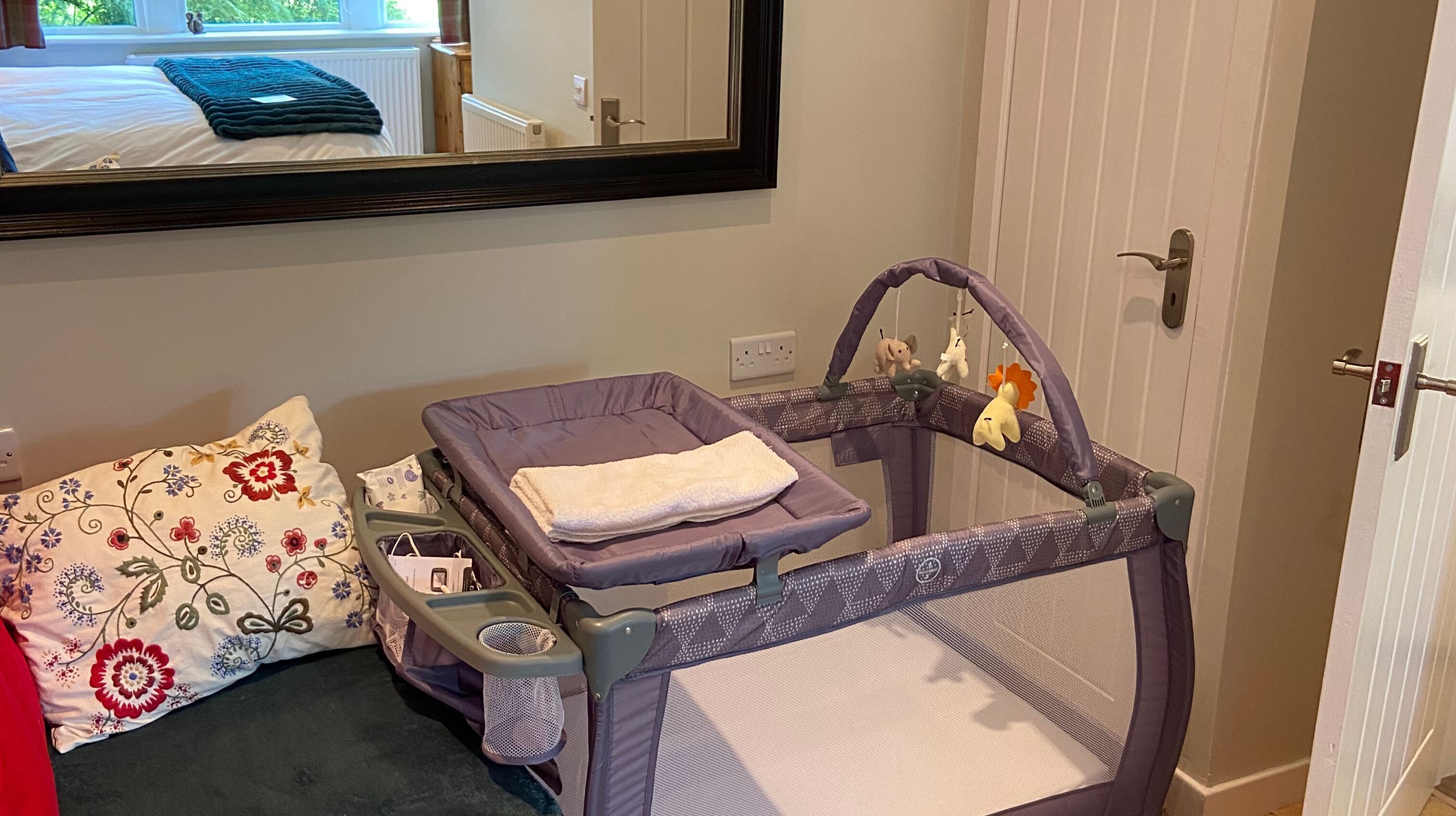 Een verschoningstafel voor baby's met een paars onderstel, een witte handdoek en een hangend speeltje.