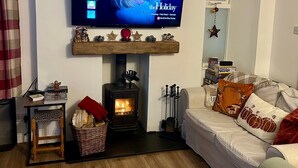 Una sala de estar acogedora con chimenea, un televisor montado sobre ella y un sofá con cojines decorativos.