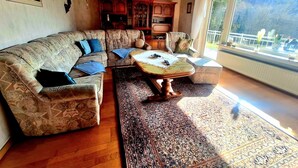 A living room with a patterned sofa, a coffee table, and a large window with a view of a mountain. - Charming, family-friendly vacation apartment in the heart of the Volcanic Eifel (Niederstadtfeld)
