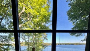 Una bandeja de madera con una botella de champán, dos copas y un libro en un alféizar con vista a un lago.