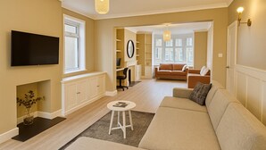 A living room with a sofa, a TV, a desk with a chair, and a window. - Stunning 5 bed house in enviable location (Bath)