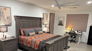 A bedroom with a large bed, bedside tables, a desk, and a ceiling fan.