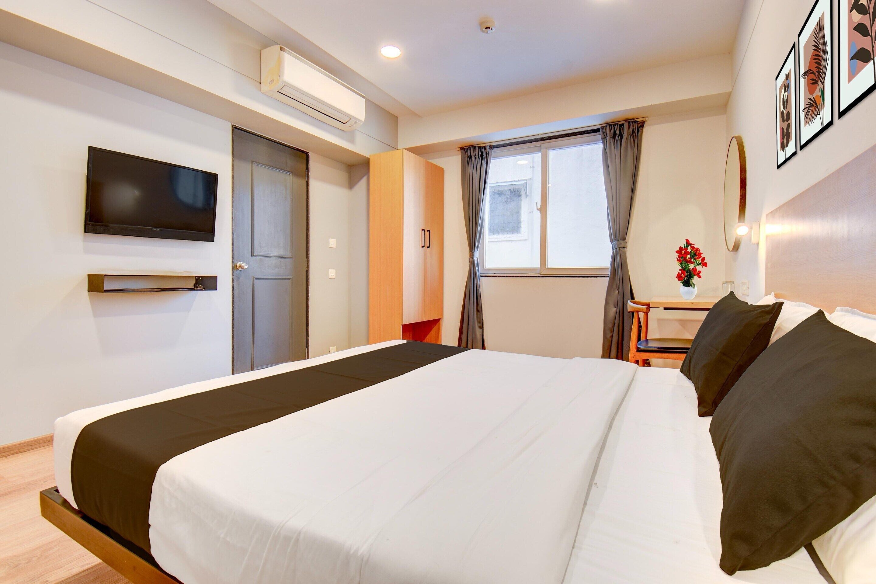Una camera d'albergo con un letto, una TV, una scrivania e una finestra con tende.