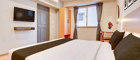 Una camera d'albergo con un letto, una TV, una scrivania e una finestra con tende.
