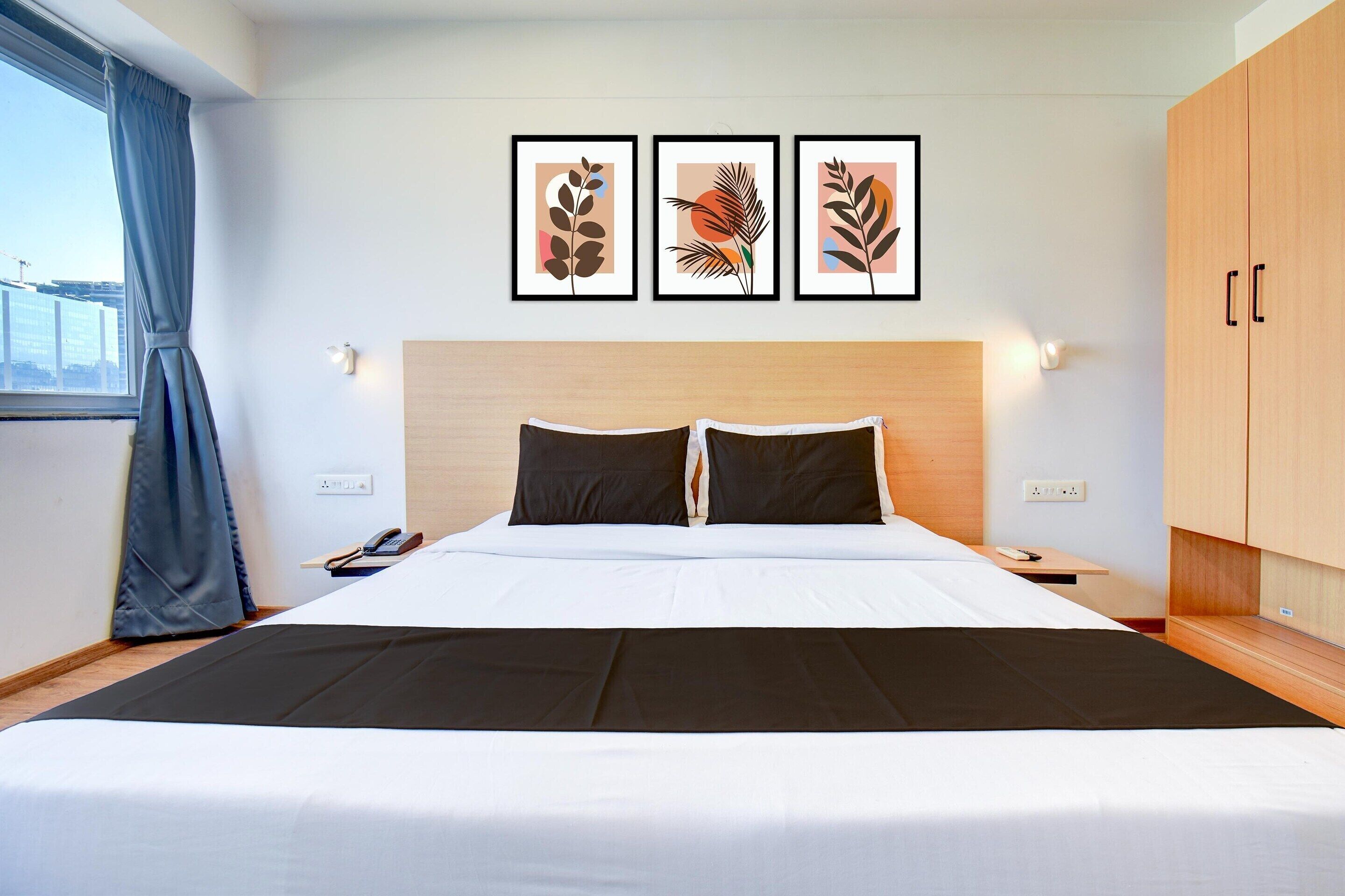 A hotel room with a large bed, a wooden headboard, a nightstand with a phone, and framed artwork on the wall.