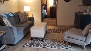 A living room with a grey sofa, a white ottoman, a grey armchair, a patterned rug, and a wooden floor. - Waterfront Home on Chadakoin River! 10 minutes to Chautauqua Lake! (Jamestown)