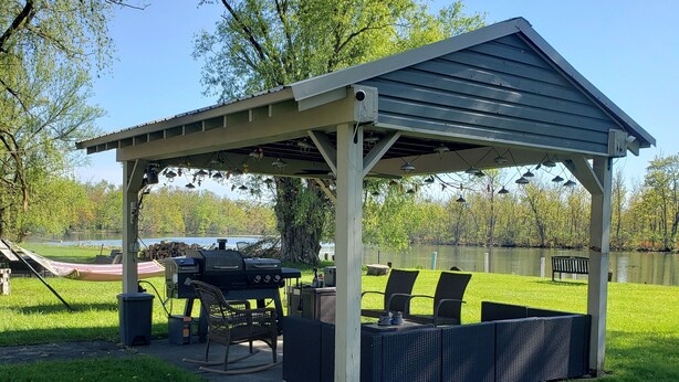A covered outdoor seating area with a grill, chairs, and a table. - Waterfront Home on Chadakoin River! 10 minutes to Chautauqua Lake! (Jamestown)