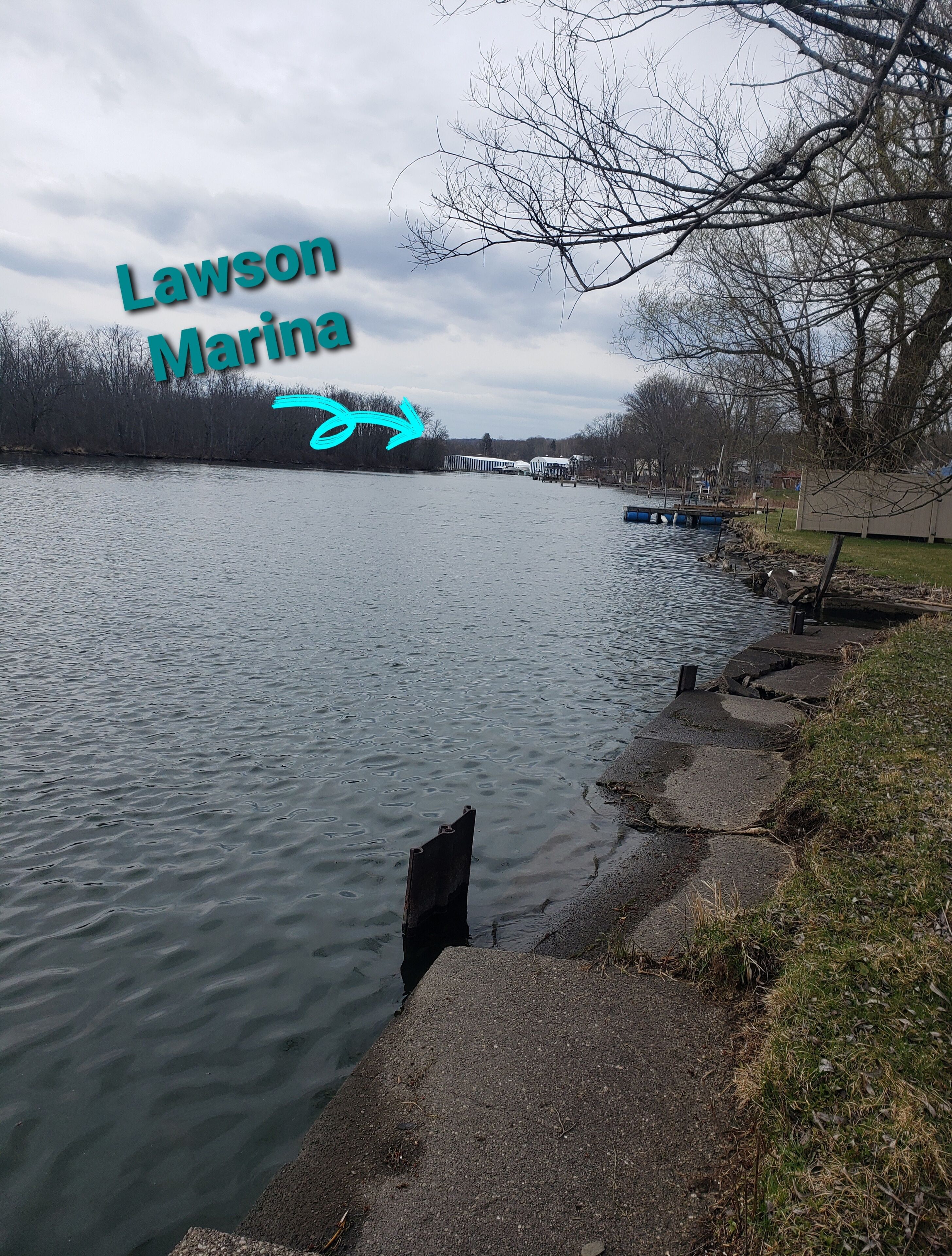 A riverside walkway with a view of the river, trees, and a distant marina.