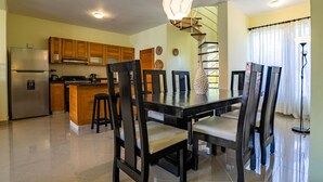 A modern kitchen with wooden cabinets, a stainless steel refrigerator, and a dining area with a black table and chairs. - Pro Cab Paradise Condos Cabarete (Cabarete)