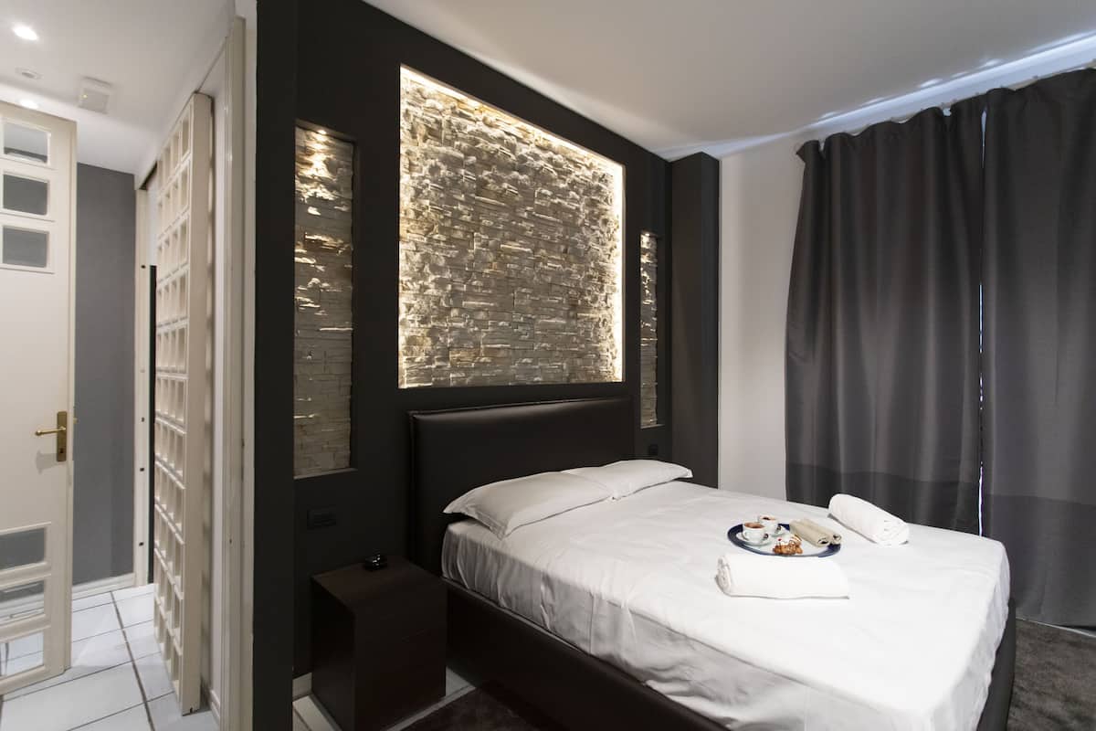 A modern hotel room with a large bed, a built-in wall feature, and a view of the city through the window.