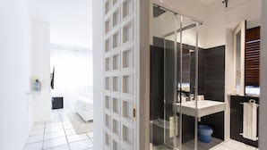 Une salle de bain moderne avec une douche à parois de verre, un lavabo blanc et un mur recouvert de carreaux foncés.