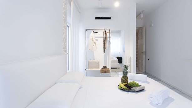 Une chambre d’hôtel moderne avec un grand lit, une petite table avec des fruits et des serviettes, et une vue sur le couloir et une autre chambre.