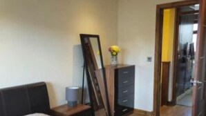 Une chambre à coucher moderne avec un grand lit, une commode, un miroir et un vase rempli de fleurs.