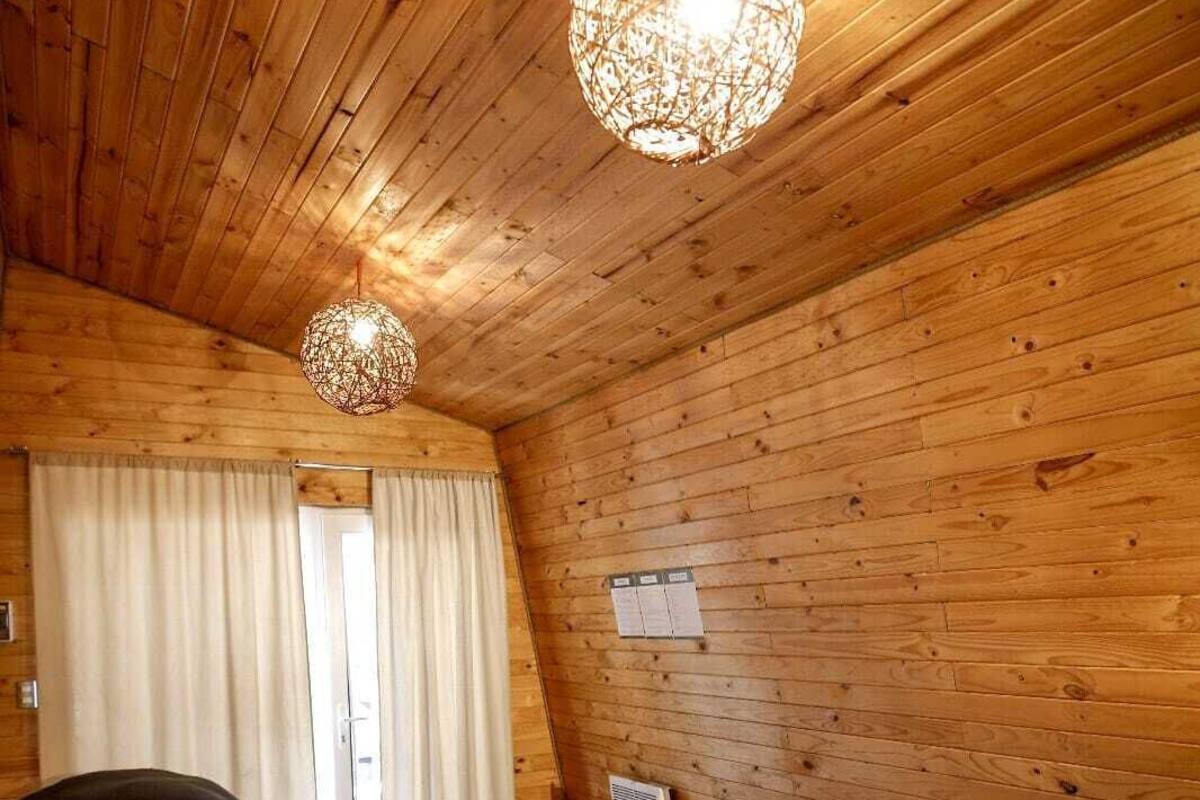 A wooden cabin room with two beds, a hanging light fixture, and a window with curtains.