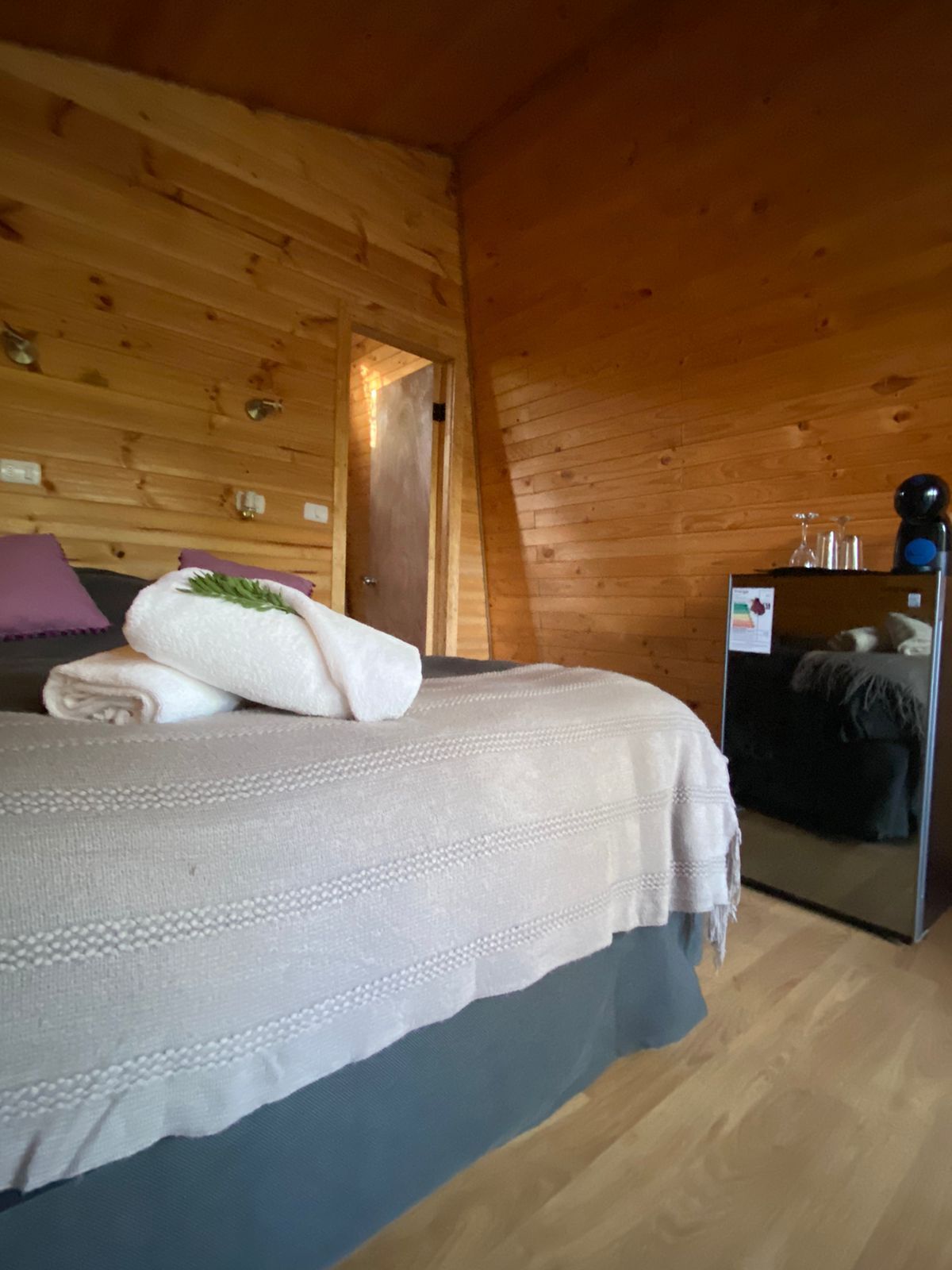 A wooden cabin bedroom with a bed, pillows, and a mirror.