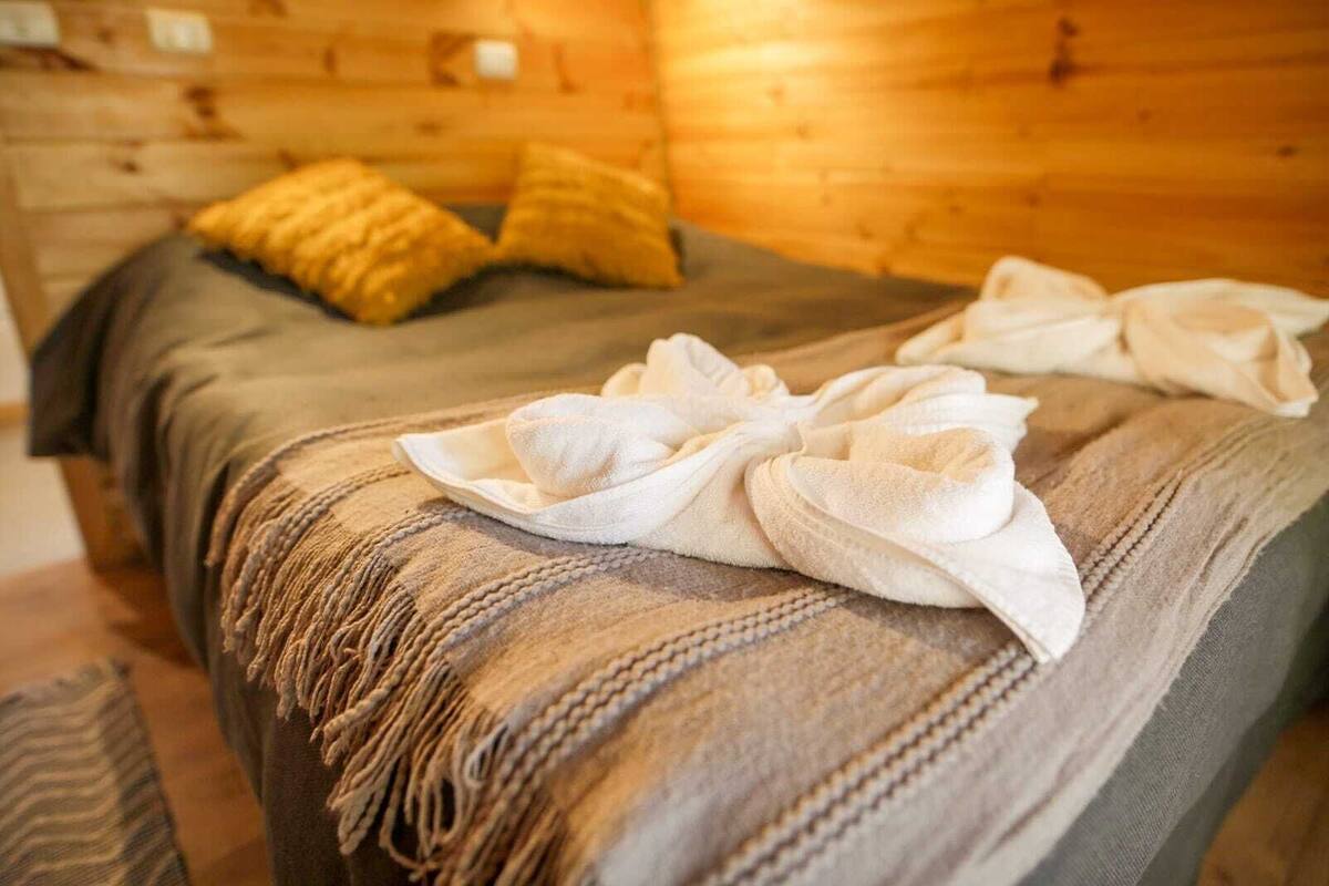 A wooden cabin room with a bed, pillows, and towels.