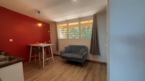 A compact living space with a kitchenette, a dining table with chairs, a grey sofa, and a window with curtains. - Cannelle, Sea View, shared pool Mont Vert Les Bas (Montvert)