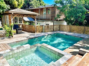 Ein Garten mit Schwimmbad, einer Holzterrasse und einem überdachten Sitzbereich.