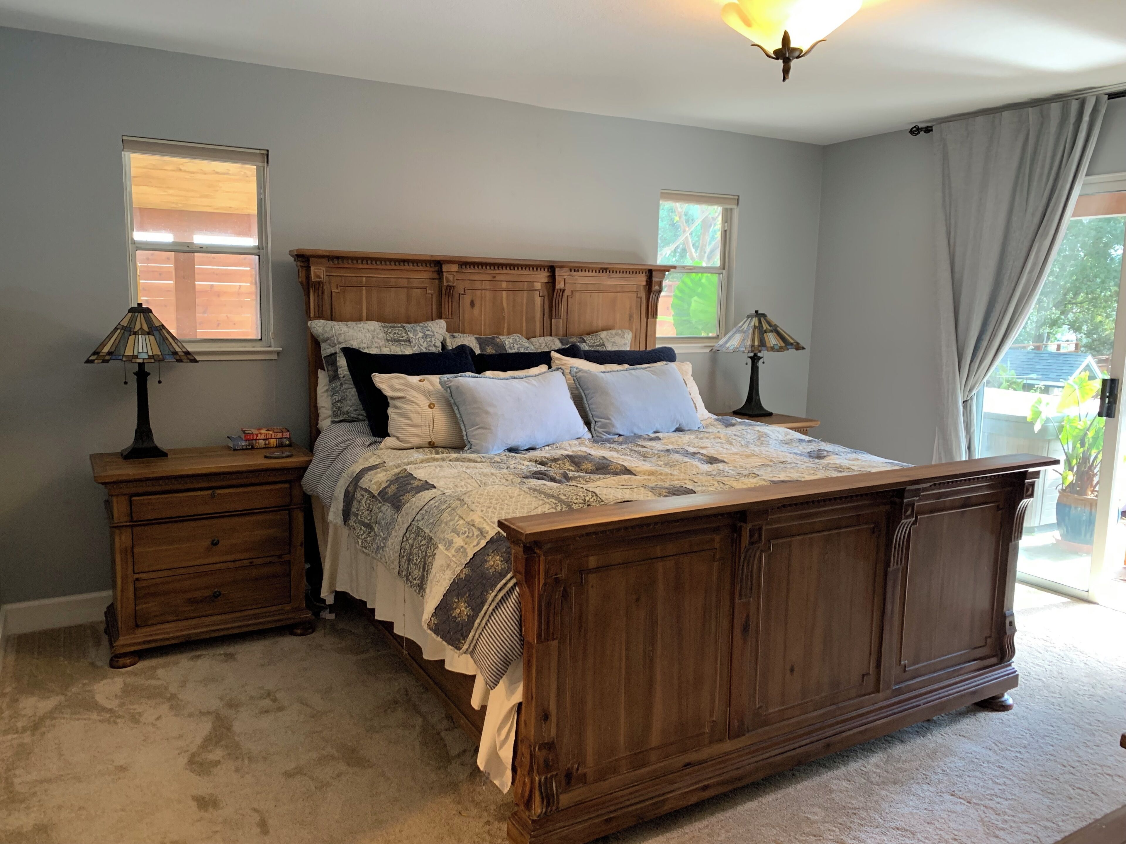 A bedroom with a large wooden bed, two nightstands, a dresser, and a window with curtains.