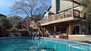 A two-story house with a pool, wooden deck, and outdoor furniture.
