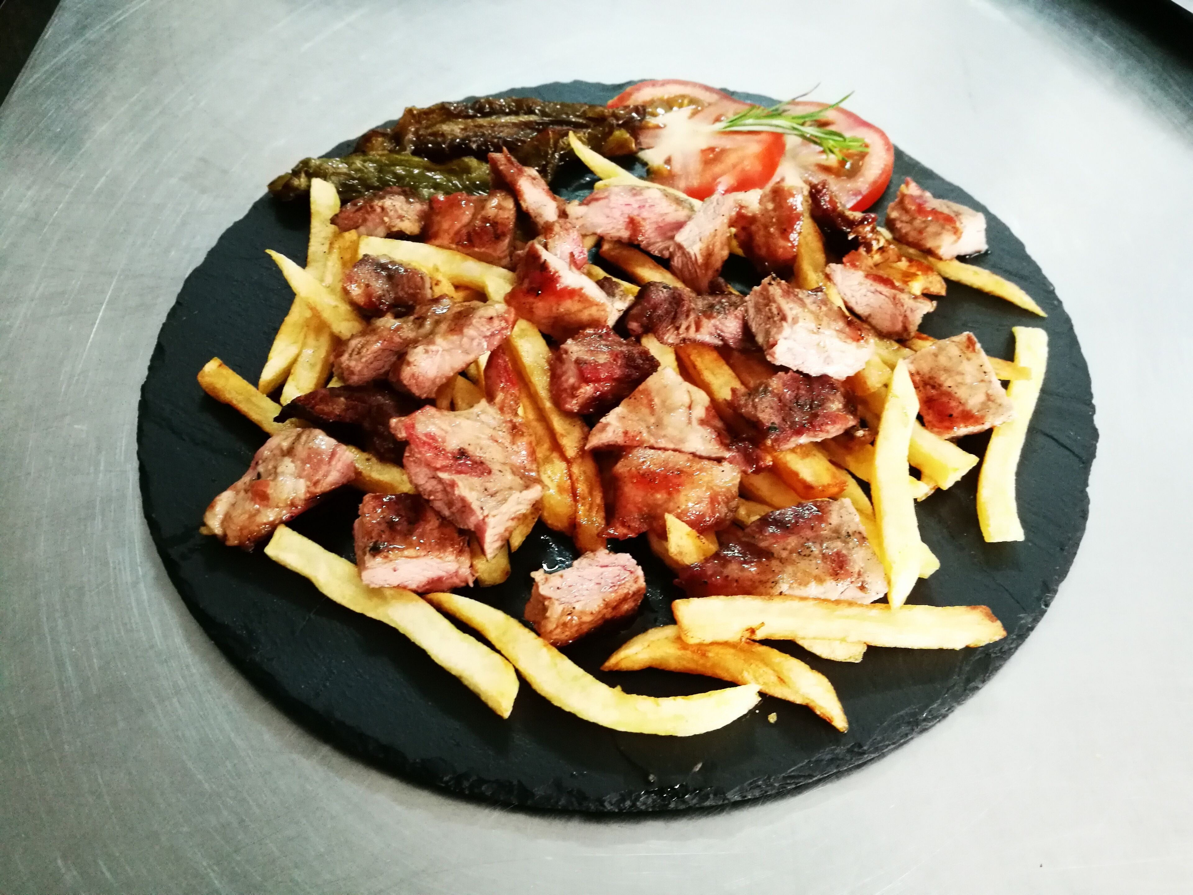 A plate of food with steak and fries on a black slate.