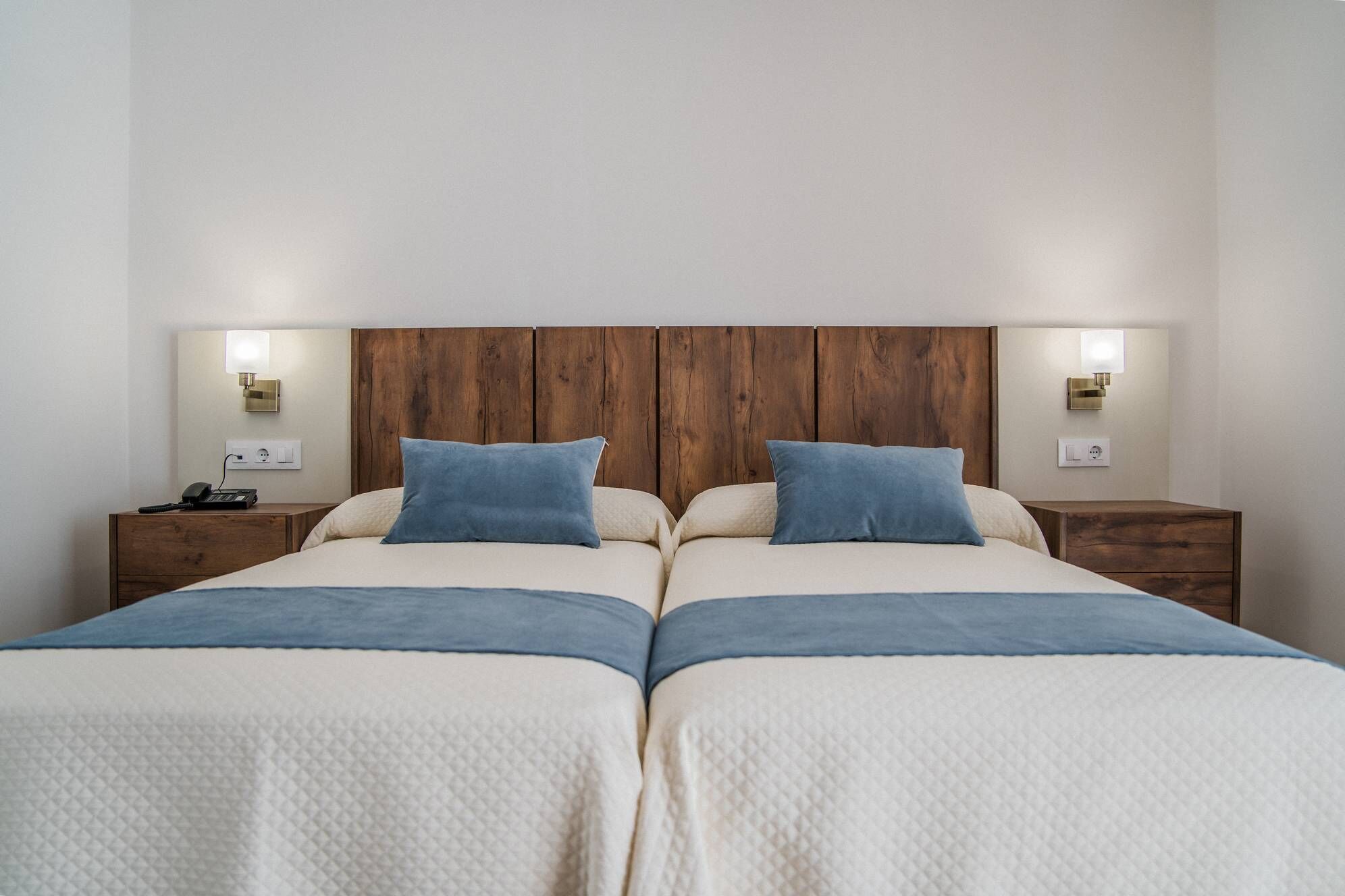 A double bed with a wooden headboard, two bedside tables with lamps, and a power outlet on the wall.