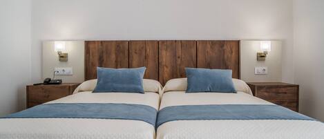 A double bed with a wooden headboard, two bedside tables with lamps, and a power outlet on the wall.