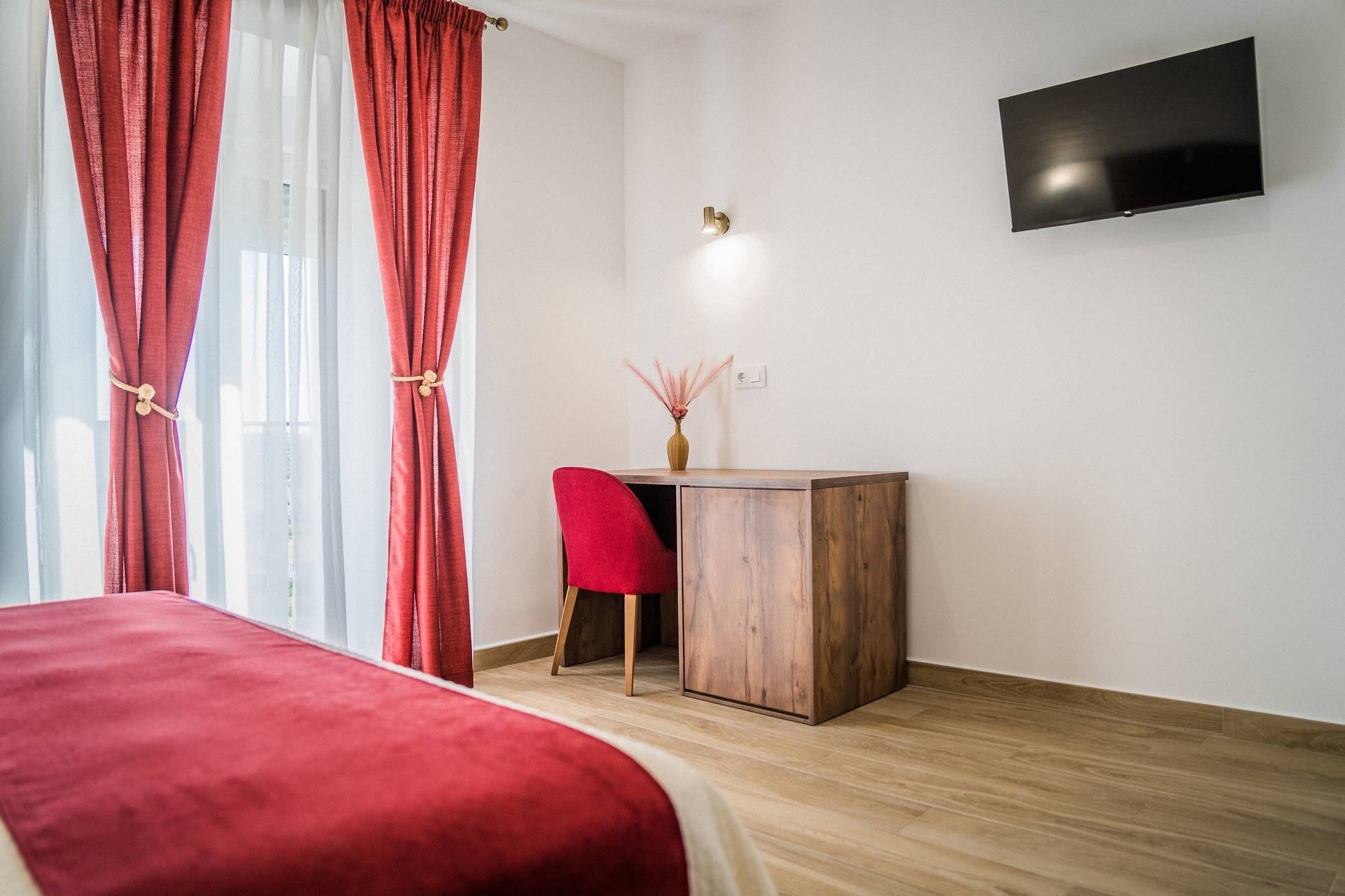 Une chambre d’hôtel avec un lit, un bureau et une chaise, un vase et un téléviseur à écran plat fixé au mur.