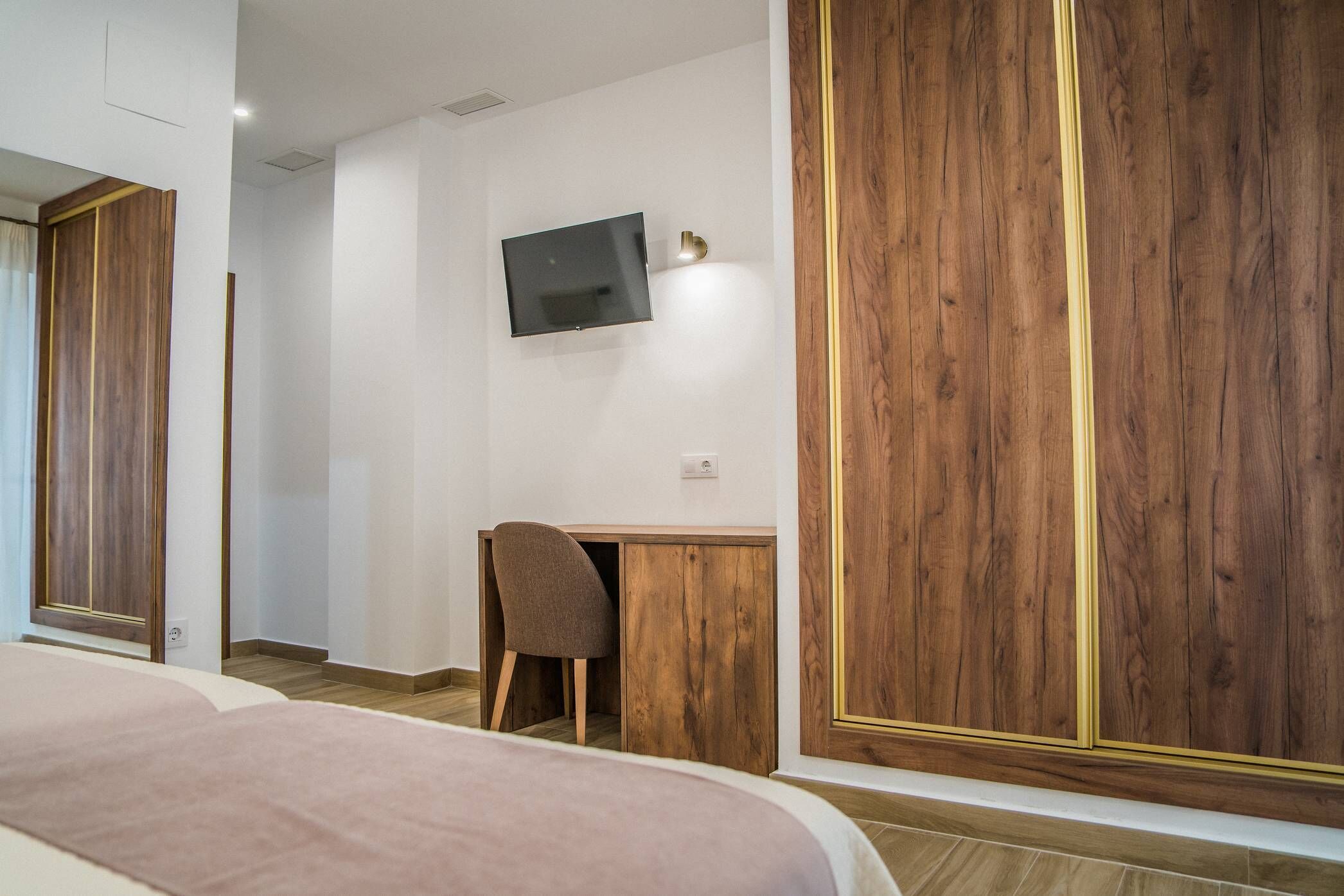 Un dormitorio con cama, escritorio, silla y televisor montado en la pared.