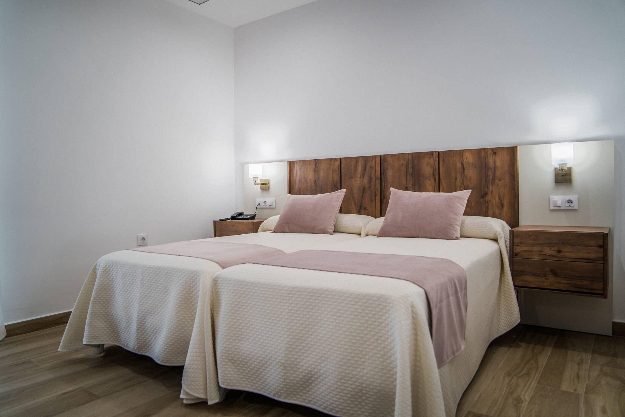Una cama doble con cabecera de madera, dos mesitas de noche y un buró.