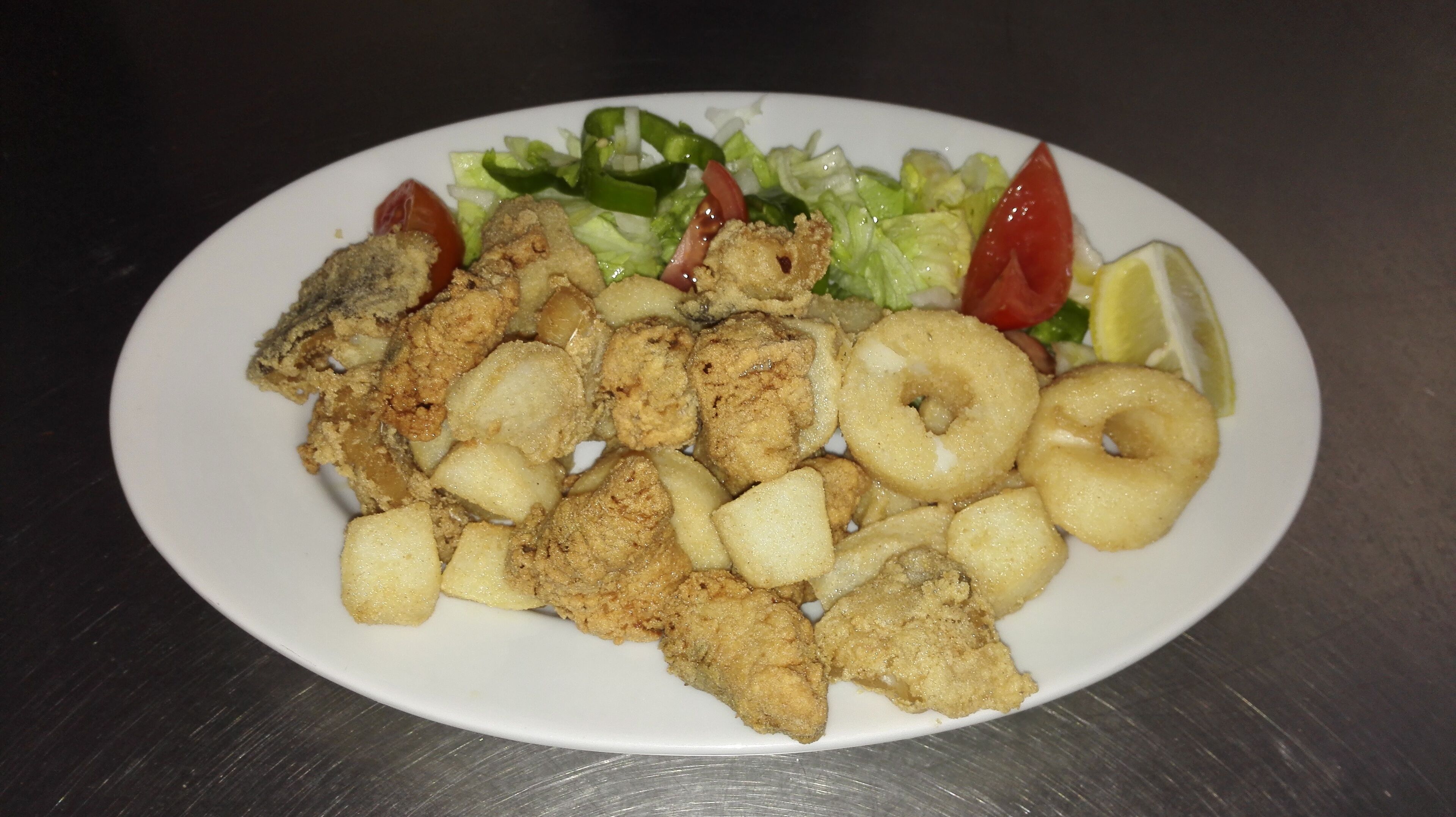 Un plato de comida frita con vegetales y una rodaja de limón.