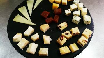 Una tabla redonda de pizarra negra con varios tipos de queso y fruta dispuesta sobre ella.