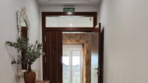 A hallway with a wooden floor, a white console table with a potted plant, a door with a stone wall, and a sign reading "SALIDA". - HOTEL RURAL LA TEJA (Segura de León)