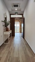 Un pasillo con piso de madera, una mesa consola blanca con una planta en maceta, una puerta con pared de piedra y un letrero que dice "SALIDA".