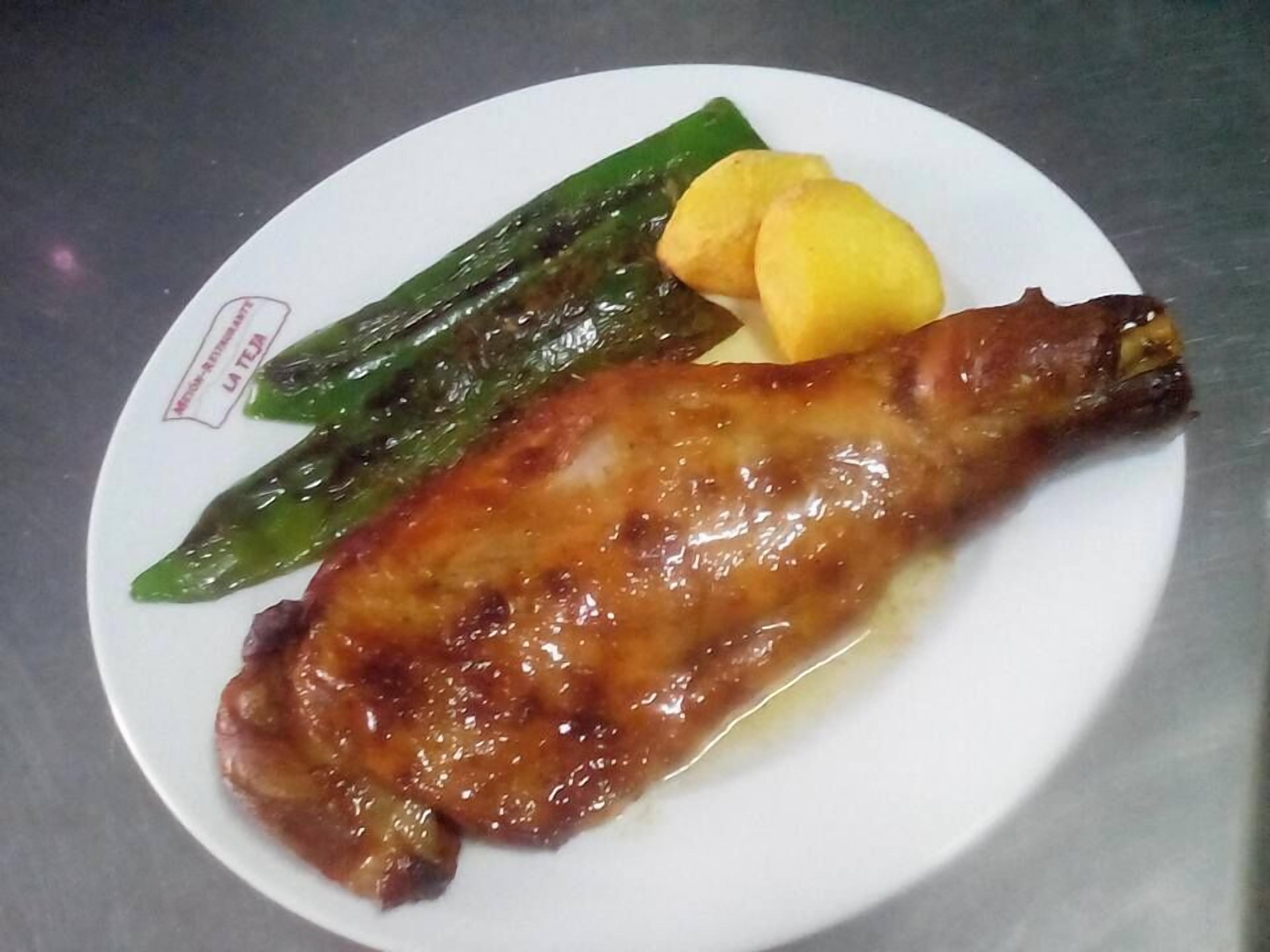 Un plato con pierna de carne asada, verduras verdes y patatas amarillas.