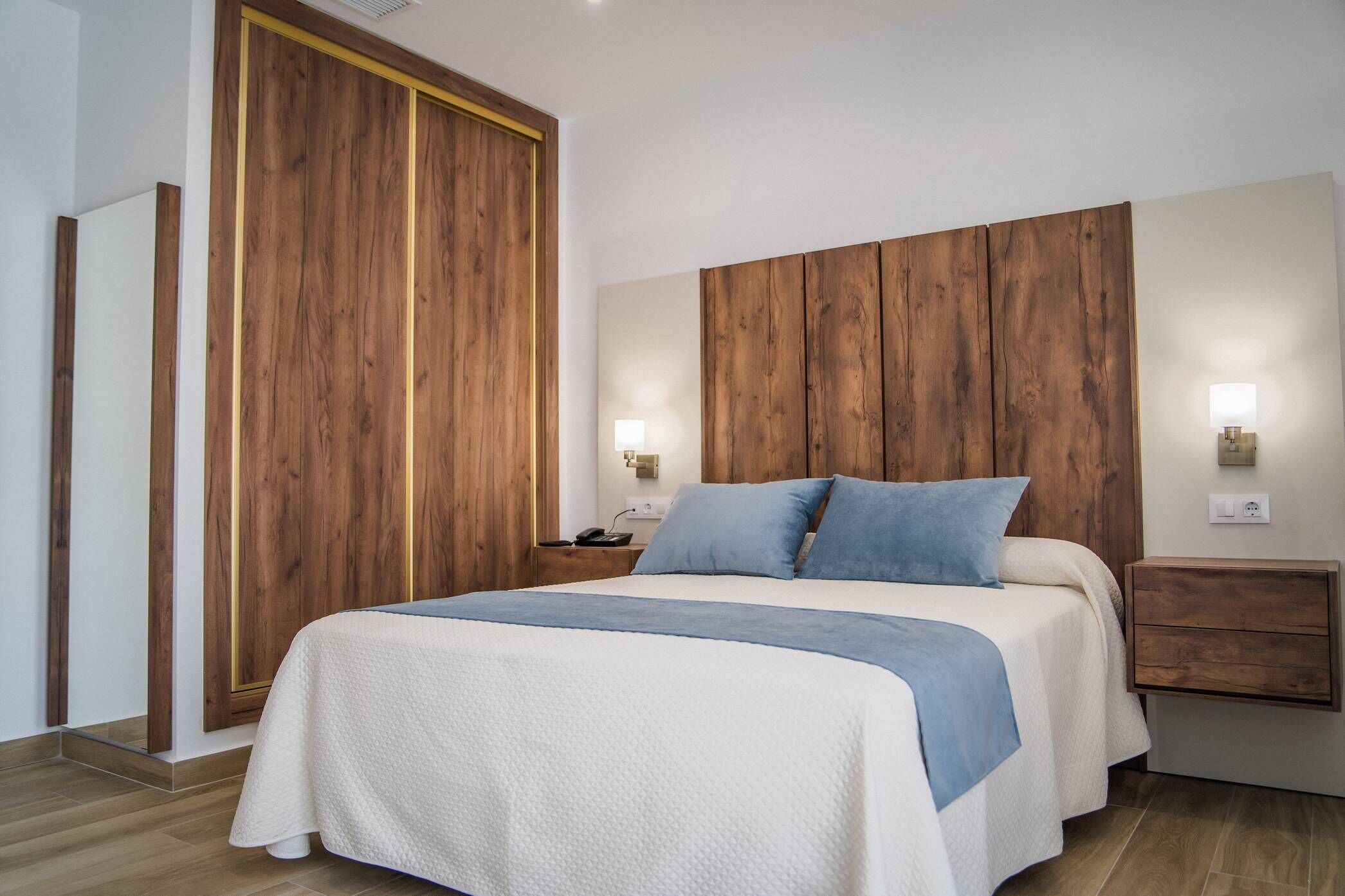 A bedroom with a large bed, wooden headboard, bedside tables with lamps, and a wardrobe.