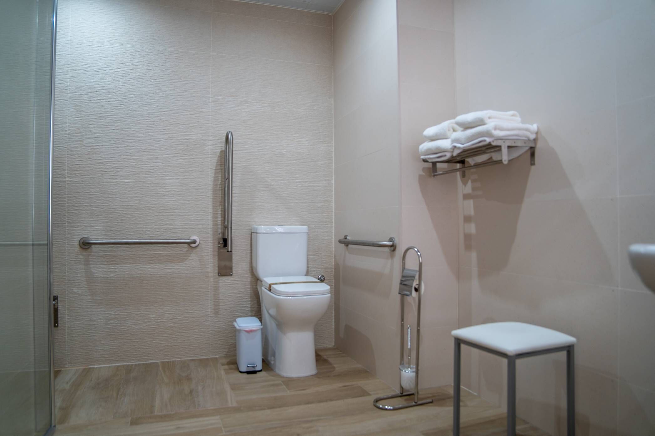 Casa de banho moderna com sanita, barra de apoio, um pequeno cesto de lixo e um porta-toalhas.