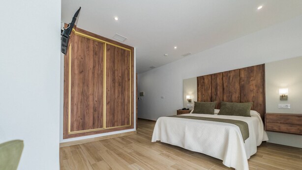A modern bedroom with a wooden wardrobe, a large bed with a white and green bedspread, and a nightstand with a lamp. - HOTEL RURAL LA TEJA (Segura de León)