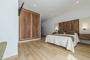 A modern bedroom with a wooden wardrobe, a large bed with a white and green bedspread, and a nightstand with a lamp. - HOTEL RURAL LA TEJA (Segura de León)