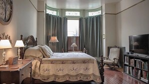 A bedroom with a bed, bedside lamps, a chair, a television, and a bookshelf. - Rustic Charm / King Bed + Roku / Private Bath (Shamokin)