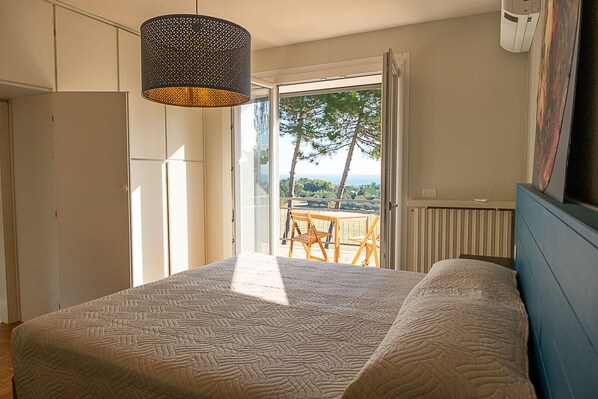 A bedroom with a bed, a hanging light fixture, a sliding glass door leading to an outdoor area with a table and chairs, and a radiator on the wall. - Bea&Berto - B&B (Pesaro)