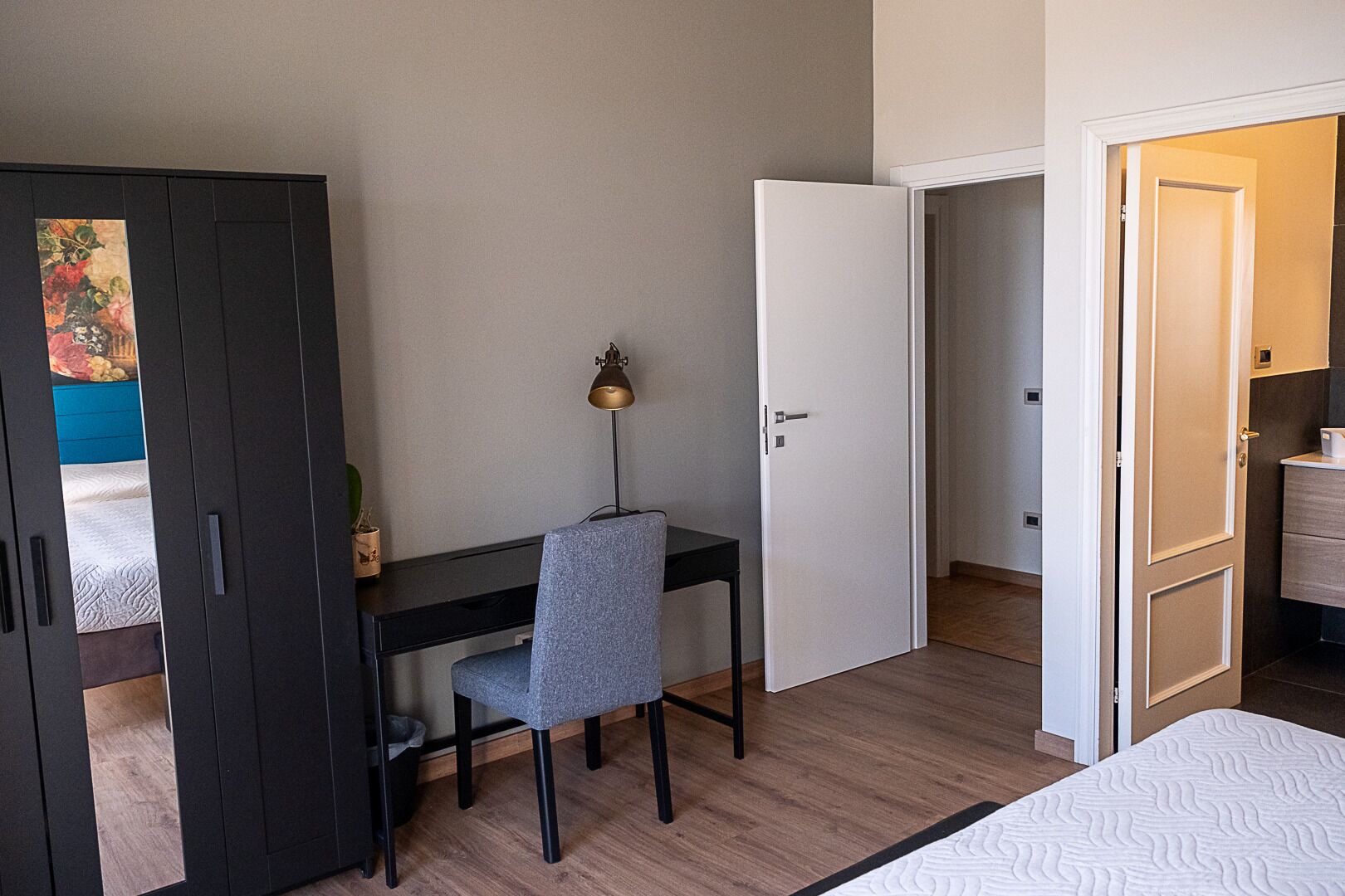 Un dormitorio con una cama, un escritorio con silla, un armario y una puerta que da a otra habitación.