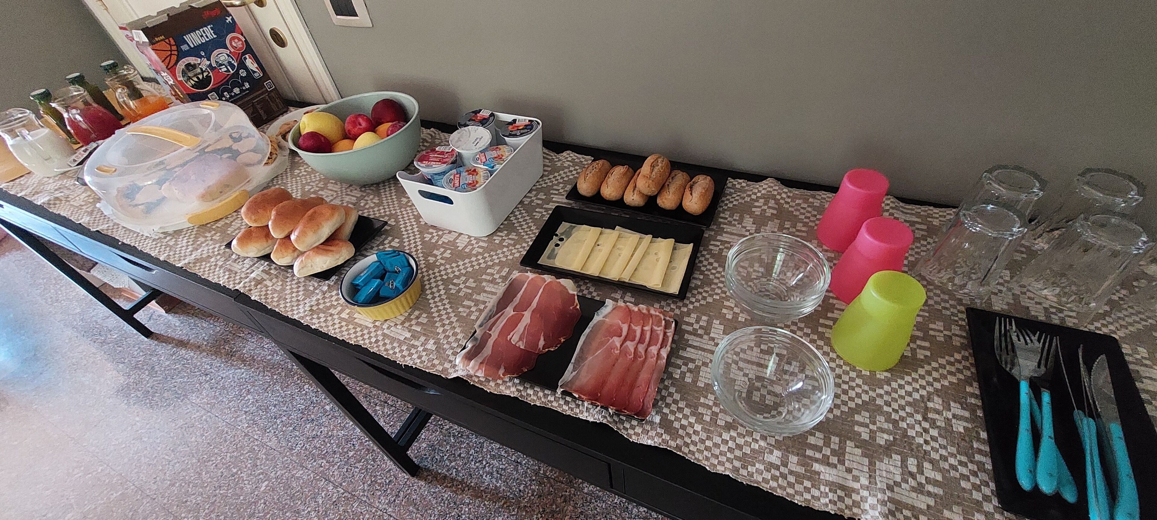 A table with various food items, including bread, pastries, and meat, along with condiments and drinks.