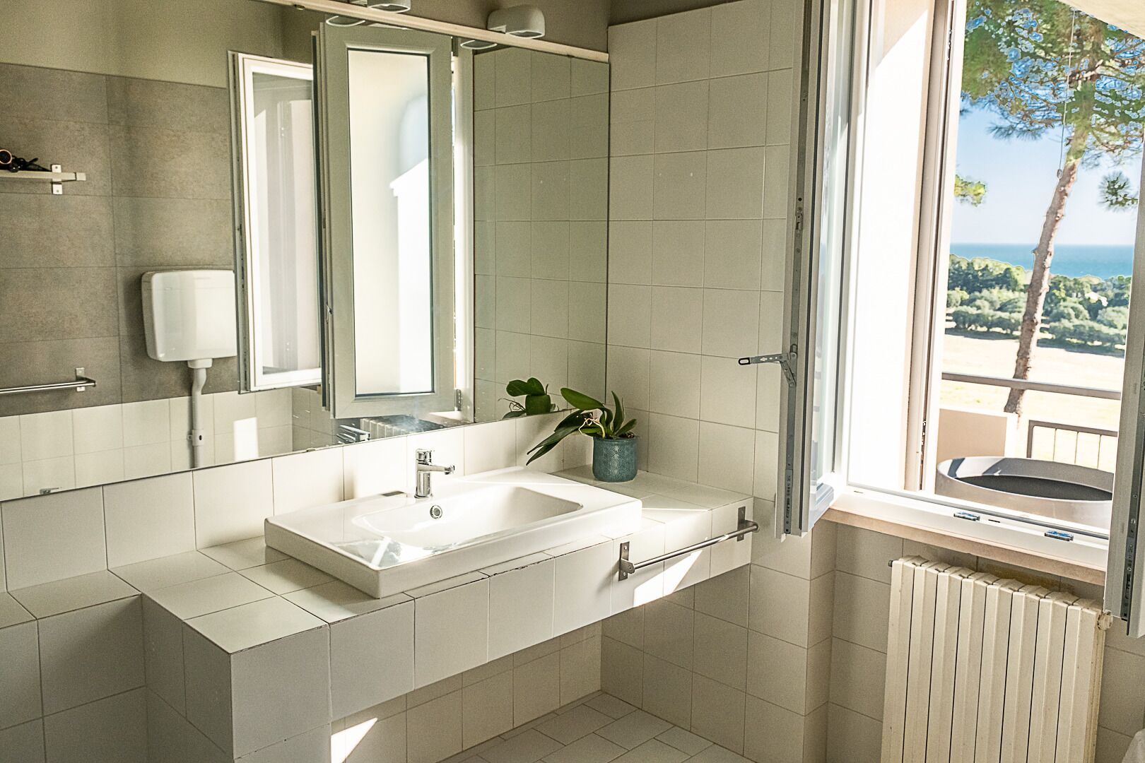 A modern bathroom with a large window, a sink, a mirror, and a potted plant.