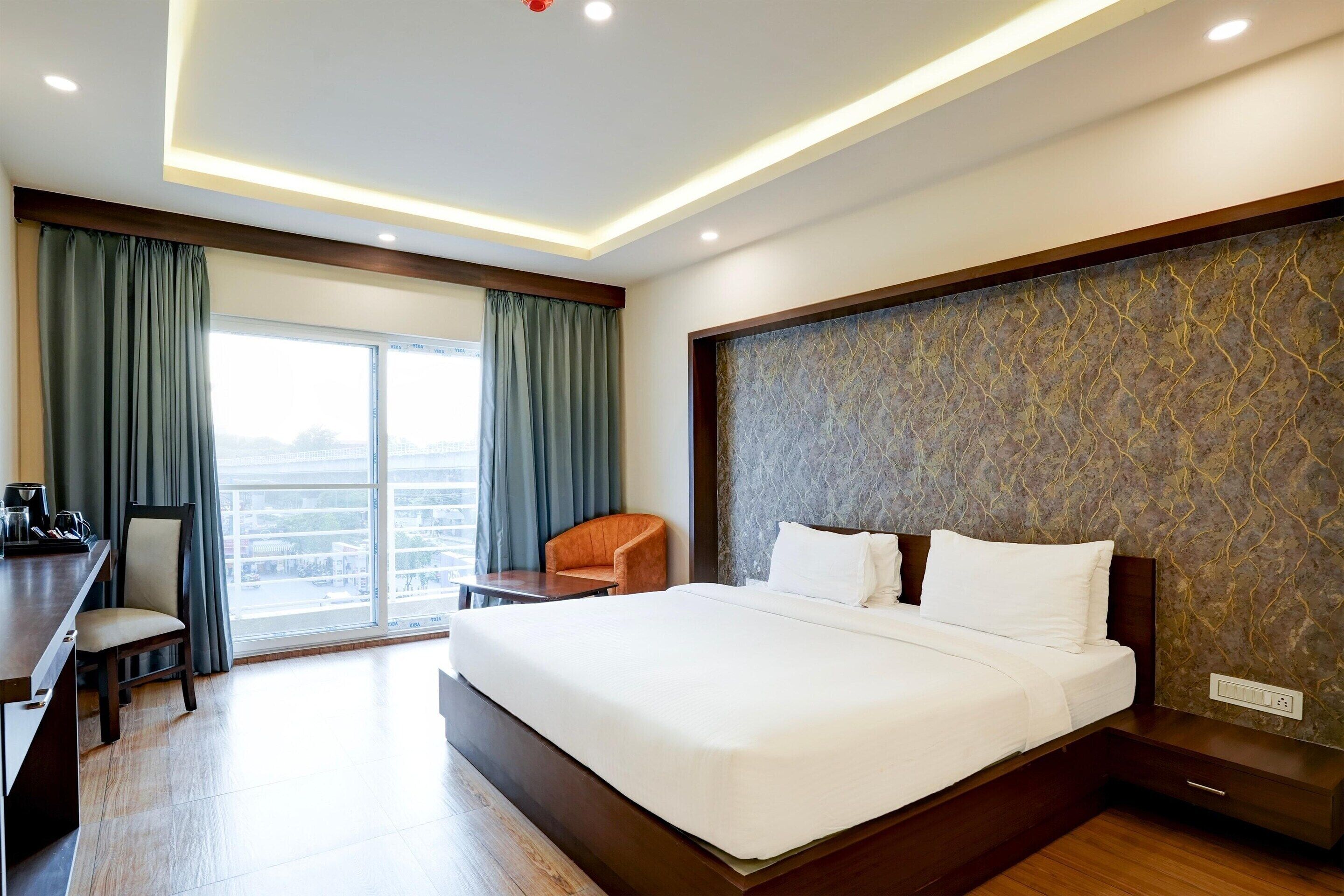 A hotel room with a large bed, a desk, a chair, and a view of the city through the window.